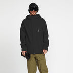 A man modeling a black hooded snowboard jacket, olive green snow pants, black goggles, and black snow boots against a light gray studio background.