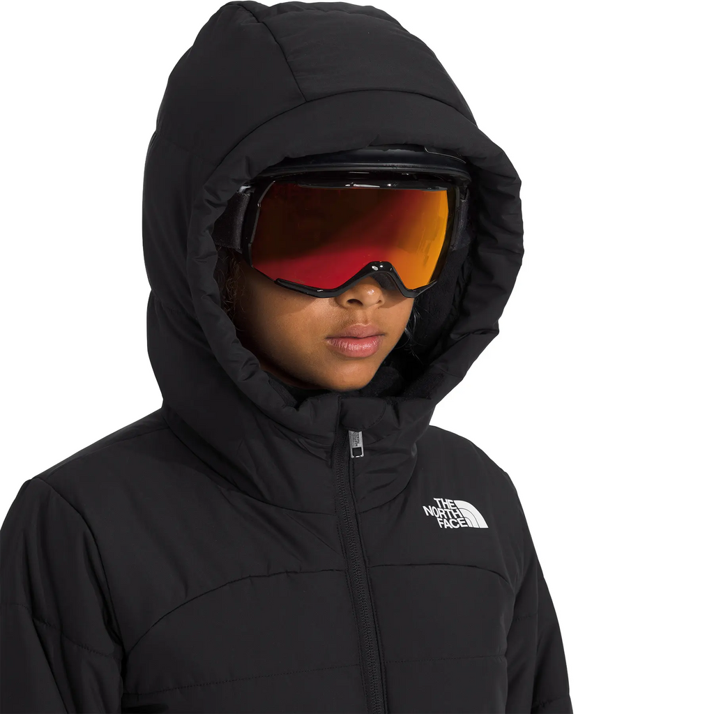 A close-up of a person wearing a black hooded winter jacket and ski goggles with a red-orange mirrored lens. The jacket features a white embroidered logo on the left chest, which is The North Face.