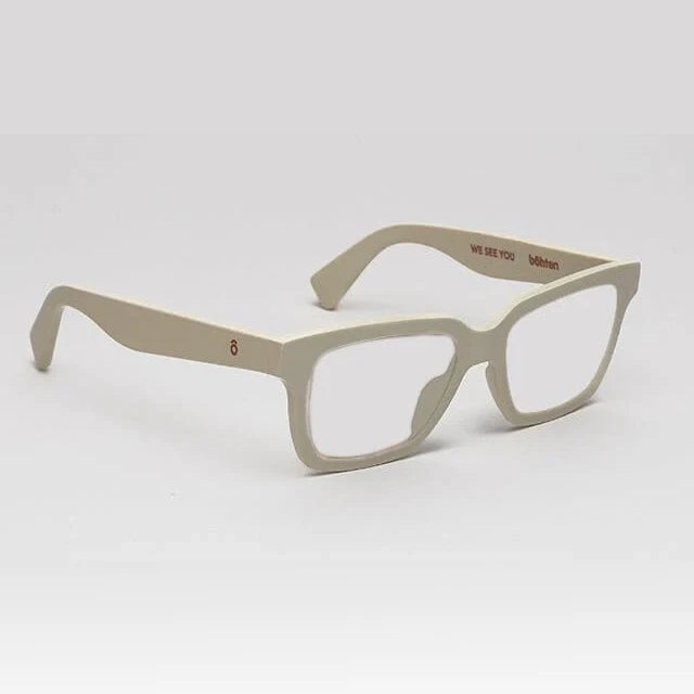 A pair of matte beige square-frame eyeglasses with clear lenses, displayed on a clean light gray background. The brand name 'Mikron' is printed in brown on the inner temple arm alongside the text 'WE SEE YOU'.