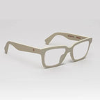 A pair of matte beige square-frame eyeglasses with clear lenses, displayed on a clean light gray background. The brand name 'Mikron' is printed in brown on the inner temple arm alongside the text 'WE SEE YOU'.